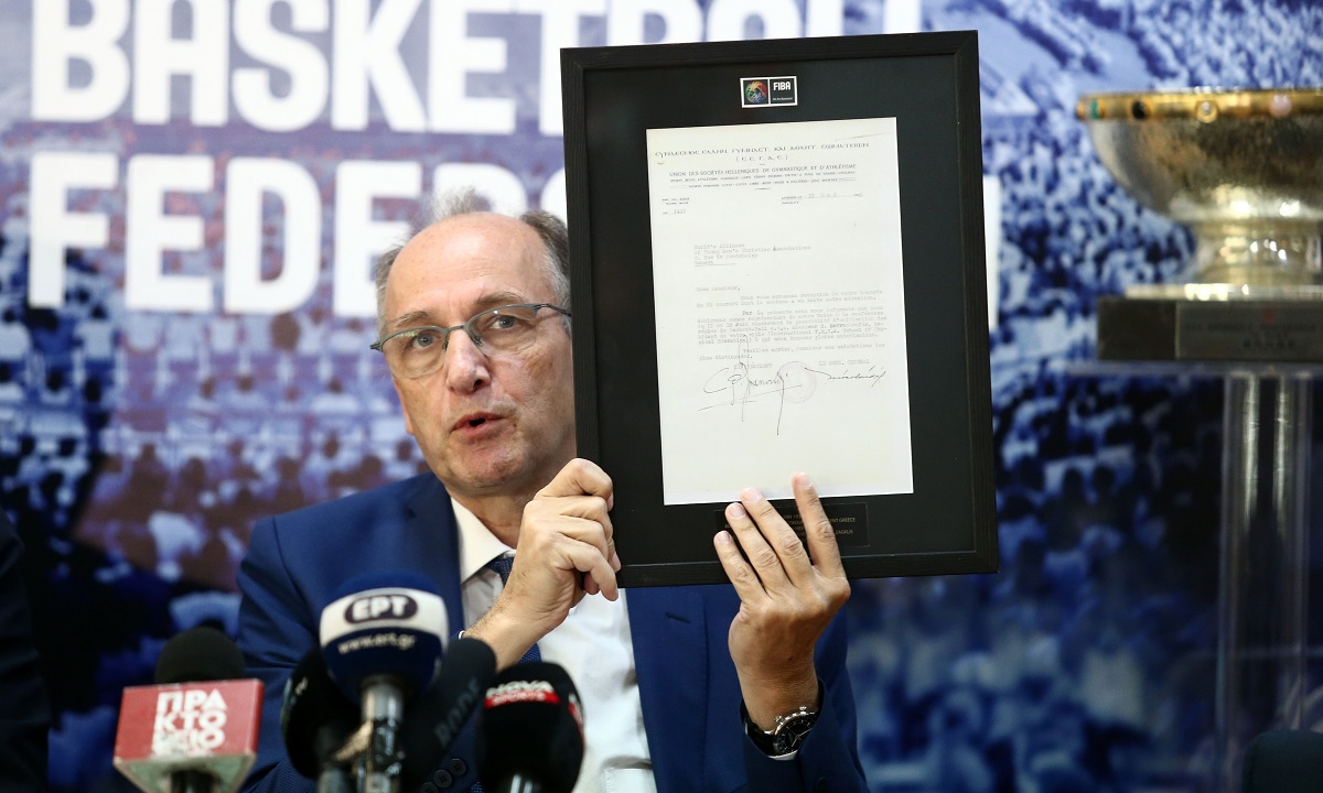 Στη φωτογραφία που επιλέξαμε ο πρόεδρος της ΕΟΚ, Βαγγέλης Λιόλιος κρατά την πρόσκληση της FIBA (το 1932) προς τον ιστορικό παράγοντα του μπάσκετ, Συμεών Μαυροσκούφη.